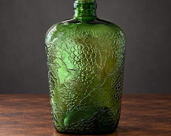 May include: A translucent emerald green glass bottle featuring a raised, embossed texture of grape clusters and vine leaves across its entire surface. The bottle has a narrow neck with a circular opening and a rounded, slightly flattened body shape.