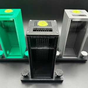 Puede incluir: Tres contenedores rectangulares y abiertos en verde, negro y gris. Cada uno tiene un interior perforado y un símbolo de diana amarillo en la parte superior. Los contenedores se asientan sobre bases negras con perillas ajustables.