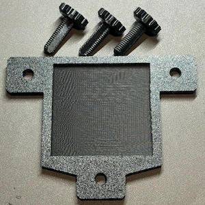 May include: A close-up shot of three black screws above a rectangular, textured, dark gray metal plate with a mesh insert. The plate has rounded corners and three holes.