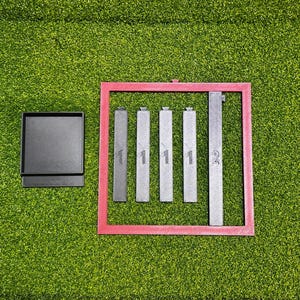 May include: An overhead shot shows a black box next to a pink rectangular frame containing five gray rectangular objects. The objects are labeled with the numbers 1 and 2. The background is green.