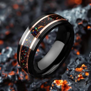 May include: Black ring with a rose gold band and a colourful opal inlay. The ring has a polished finish and a modern design. The opal inlay features a mix of red, orange, blue, and green colours.