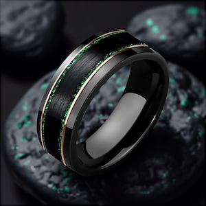 Könnte beinhalten: Ein schwarzer Ring aus Wolframcarbid mit einer grünen und roségoldenen Einlage. Der Ring hat eine gebürstete Oberfläche.