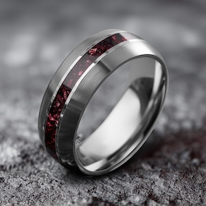 May include: A silver ring with a brushed metal finish. The ring has a central inlay of deep red, textured material, framed by polished silver bands. The design is modern and sleek, suitable for everyday wear or special occasions.