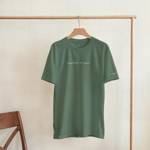 Puede incluir: Camiseta verde oliva con el texto "retrain(data:'self_worth')" en blanco. La camiseta de manga corta est&aacute; colgada de una percha de madera. La camiseta est&aacute; hecha de un material suave.