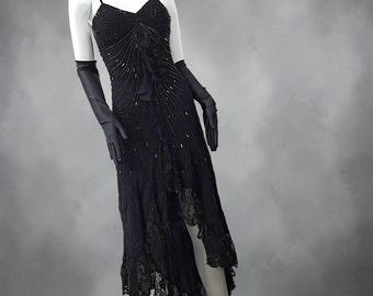 May include: A black sleeveless dress featuring intricate beadwork and sequins arranged in a radiating pattern across the bodice. The garment includes a ruffled center detail, a high-low hemline finished with black lace trim, and matching long black gloves.