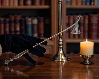 Könnte beinhalten: Eine brennende Kerze in einem goldfarbenen Halter steht neben einem hohen, verzierten Kerzenhalter. Eine Hand in einem schwarzen Handschuh hält einen Kerzenlöscher und einen Dochtschneider. Im Hintergrund ein Bücherregal voller Bücher.