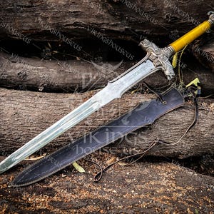 May include: A silver-toned metal sword with a double-edged blade, a detailed crossguard featuring animal head motifs, and a yellow-wrapped handle topped with a decorative pommel. A black leather scabbard with thin brown leather straps lies below.