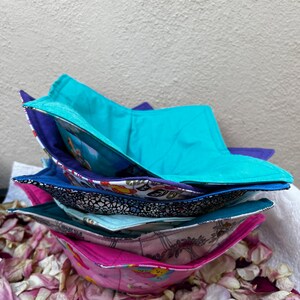 May include: A stack of five colourful fabric bowls with different patterns. The bowls are folded and stacked on top of each other. The bowls are sitting on a bed of pink rose petals.