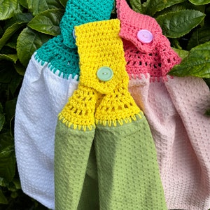 May include: Three crocheted dish towels with different coloured borders and buttons. The towels are green, yellow and pink.