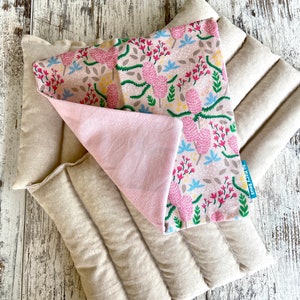 May include: Two beige, rectangular, quilted heating pads with a floral patterned fabric on top. The floral fabric has pink, blue, and green accents on a tan background. A pink fabric is visible underneath the floral fabric. The text "So Mary Sews" is visible.
