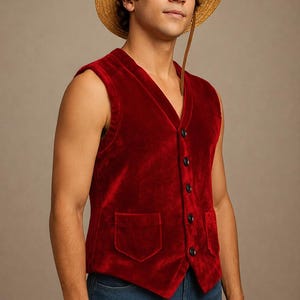 May include: A red velvet vest with a V-neck and black buttons. The vest has two pockets and is paired with blue jeans. A straw hat with a brown strap completes the look.