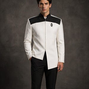 Pode incluir: Casaco branco com detalhes pretos nos ombros e gola preta, combinado com calças pretas. O casaco tem fecho de correr e um pequeno emblema no peito. O conjunto é uma versão moderna de um uniforme clássico.
