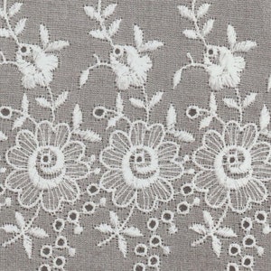 May include: White cotton fabric with a delicate embroidered floral pattern. The fabric has a scalloped edge and small holes throughout.