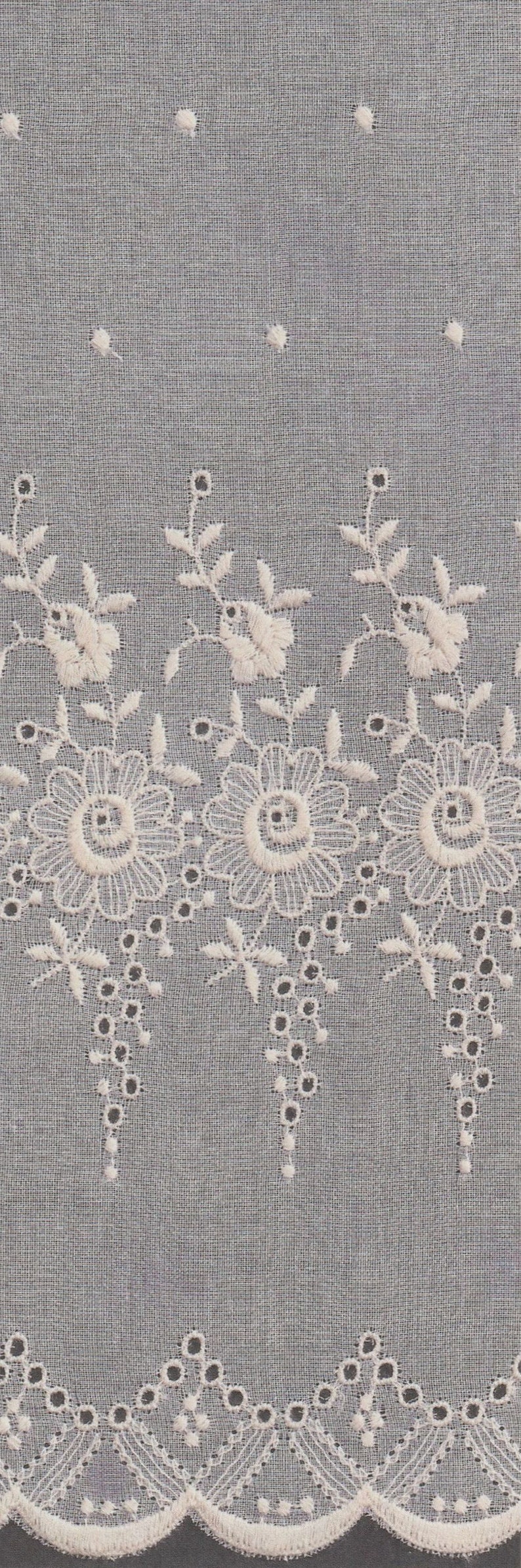 May include: White cotton fabric with a delicate embroidered floral design. The embroidery features small flowers and leaves with a scalloped edge.
