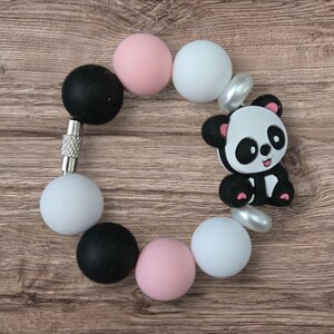 May include: A baby bracelet featuring a panda bear charm and colorful beads. The bracelet includes black, white, and pink round beads, with a silver clasp. The panda charm is black and white with pink accents.
