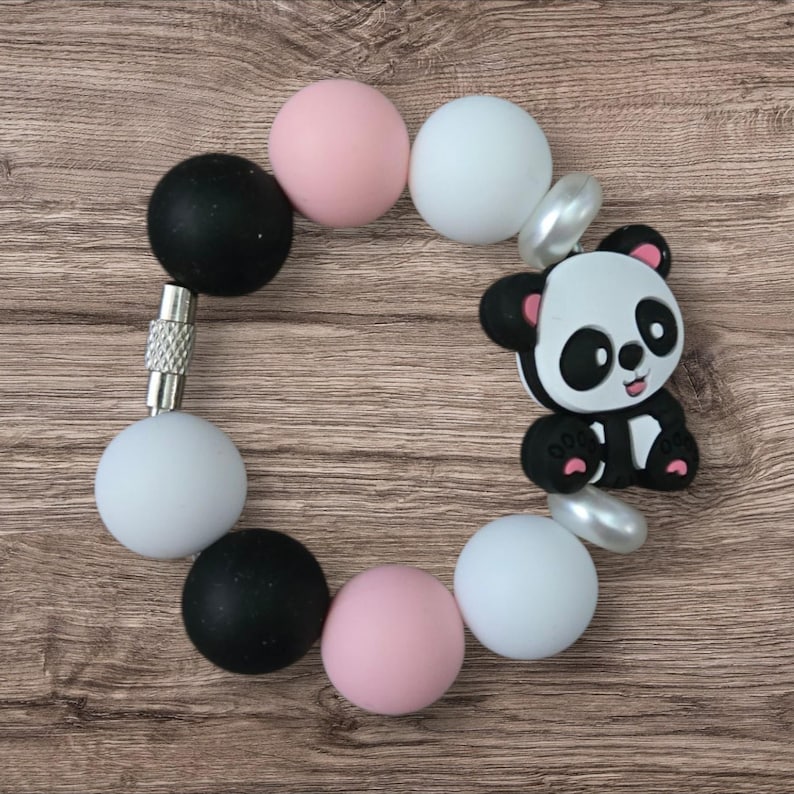 May include: A baby bracelet featuring a panda bear charm and colorful beads. The bracelet includes black, white, and pink round beads, with a silver clasp. The panda charm is black and white with pink accents.