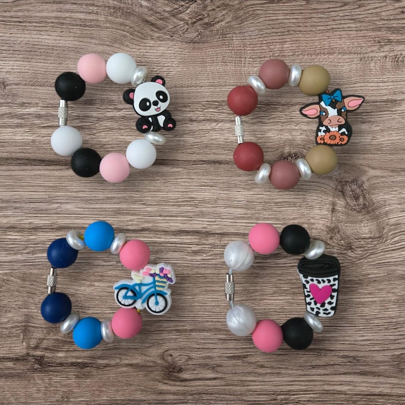 May include: Four colorful silicone bead bracelets with decorative charms. One bracelet has a panda bear charm, another has a cow, a third has a bicycle, and the last has a coffee cup with a heart.