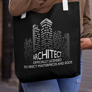 Puede incluir: Un bolso tote negro con un diseño arquitectónico blanco de edificios urbanos. El texto en el bolso dice: "ARCHITECT, OFFICIALLY LICENSED TO ERECT MASTERPIECES AND EGOS". El bolso tiene correas blancas.
