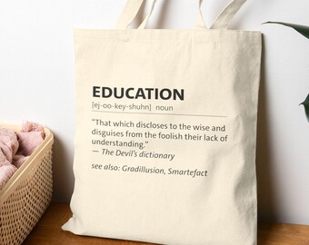 May include: A cream-colored tote bag with the word "EDUCATION" printed in black, along with a definition from "The Devil's dictionary." The bag has two handles and is made of a sturdy fabric.