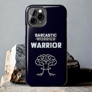 May include: A navy blue phone case with the text "SARCASTIC WORRIER WARRIOR" in white. Below the text is a white illustration of a brain with roots. The phone case has a glossy finish and a camera cutout.