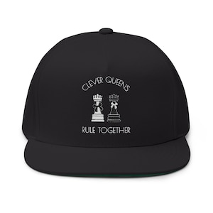 Puede incluir: Gorra de béisbol negra con visera plana y parte inferior verde. La gorra presenta el texto blanco "CLEVER QUEENS RULE TOGETHER" y dos ilustraciones de piezas de ajedrez. Un accesorio de moda.