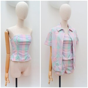 May include: A matching set featuring a strapless corset-style top, a short-sleeved button-down shirt with a collar and two front pockets, and shorts. The garments are made of a pastel gingham fabric in shades of pink, green, purple, and white.