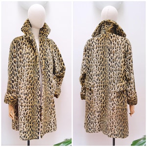 May include: A leopard print coat with a wide collar and rolled cuffs. The coat is open in the front, revealing a glimpse of the lining. The fabric features a pattern of brown and black spots on a tan background. The coat is displayed on a mannequin.