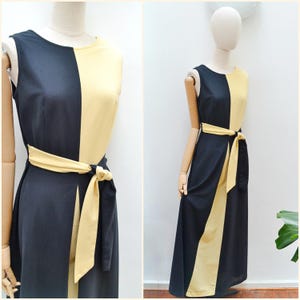 May include: Sleeveless, floor-length dress with a color-block design. The dress features a split front, a black and yellow color scheme, and a matching tie belt. The dress is displayed on a mannequin.