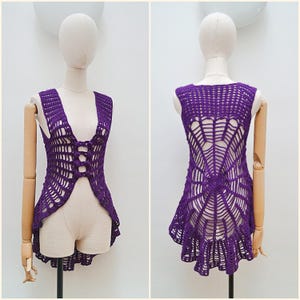 May include: A deep purple crochet vest featuring an intricate spider web pattern throughout the garment. The front displays a vertical row of four circular button closures, while the back showcases a large, detailed web design.