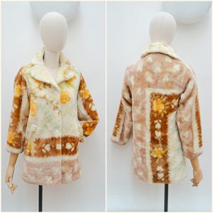 May include: A long-sleeved coat featuring a plush, textured surface with a cream, tan, and brown colour palette. The garment displays a repeating floral and geometric pattern, a wide collar, and three clear buttons down the front centre.