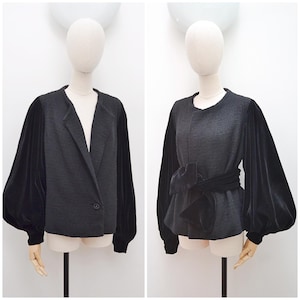 May include: A charcoal gray jacket featuring long, voluminous black velvet sleeves with fitted cuffs. The jacket has a round neckline, a single button closure, and an optional matching black velvet tie belt that wraps around the waist.