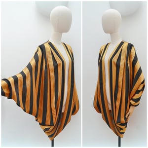 May include: A black and gold striped kimono-style jacket with a V-neck. The jacket is displayed on a mannequin, showcasing its flowing, oversized design. The fabric has a satin sheen, and the stripes are vertical.