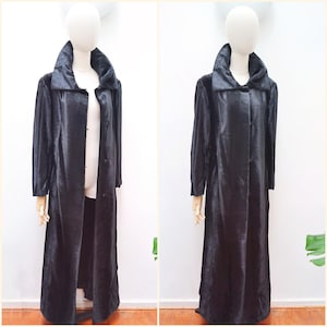 May include: A long, black coat with a wide collar and button-down front. The coat is displayed on a mannequin, showcasing its full length and design. The fabric appears to have a subtle sheen.
