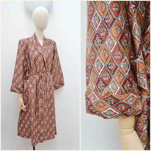 May include: A patterned robe with a belt, displayed on a mannequin. The robe features a repeating diamond pattern in shades of brown, orange, red, green, and blue. The robe has a collar, long sleeves, and pockets. The fabric appears to be lightweight.