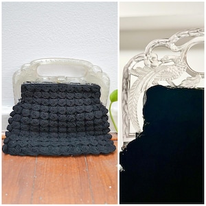 May include: A vintage black crochet handbag with a scalloped design. The bag has a clear, ornate handle and frame. The bag is displayed on a wooden surface.