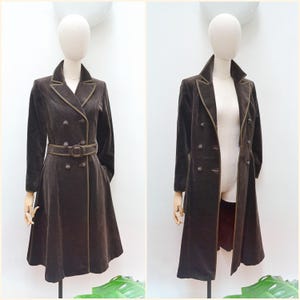 May include: A brown velvet coat with a double-breasted design, featuring a belt and contrasting trim. The coat is displayed on a mannequin, showcasing its tailored fit and classic style. The coat's length is approximately 45 inches.