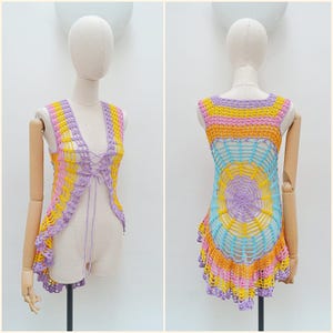 May include: A vibrant, hand-crocheted vest in yellow, pink, orange, and purple. The open-weave design has a lace-up front and a scalloped hem. The back of the vest features a circular pattern. The vest is displayed on a mannequin.
