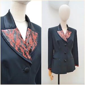 May include: A black blazer featuring a notched lapel with red and black sequin embellishments. The jacket includes a satin-finish collar, three fabric-covered buttons down the front, two side pockets with satin trim, and sequin-trimmed cuffs.