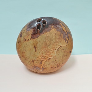 May include: A spherical ceramic vase with a mottled tan and brown glaze. The surface features a textured, earthy appearance with dark brown patches. At the top, there are three small, circular openings clustered together for holding stems.