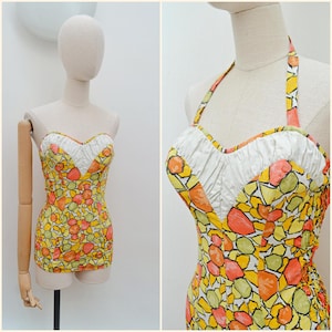 May include: Vintage halter-neck swimsuit with a colorful abstract pattern. The one-piece bathing suit features a sweetheart neckline with white fabric and a vibrant design of orange, yellow, and green shapes. The swimsuit is displayed on a mannequin.