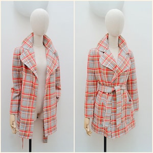 May include: A vintage plaid coat in shades of gray, red, and orange, displayed on a mannequin. The coat features a wide collar, long sleeves, and a matching belt. The coat is shown open and closed, showcasing its design.