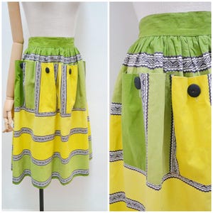 May include: A vintage skirt in shades of green and yellow, with a patchwork design and geometric patterns. It has pockets and black buttons. The skirt is high-waisted and displayed on a mannequin. The skirt's length is approximately 60 cm.