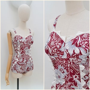 May include: A vintage-style one-piece swimsuit with a floral pattern in burgundy, white, and grey. The swimsuit features a sweetheart neckline, adjustable straps, and a ruffled trim. The garment is displayed on a mannequin.