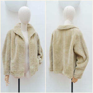 May include: A beige faux fur jacket with long sleeves and a wide collar. The jacket is shown from both the front and the back, featuring a soft, textured pile finish, a straight hemline, and an open front design without visible buttons or closures.