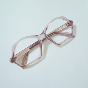 May include: Pale pink eyeglasses with a geometric frame design. The glasses have a rectangular shape with a subtle cat-eye lift. The arms of the glasses are a darker shade of pink. The text "M-1268" and "23" are visible on the frame.