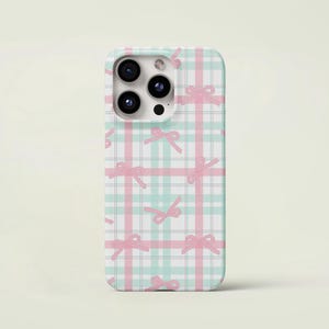 Pode incluir: Capa de telemóvel com um padrão xadrez pastel em branco, rosa e verde menta. O design inclui ilustrações de laços cor-de-rosa espalhados pela superfície. A capa tem um recorte para a câmara.