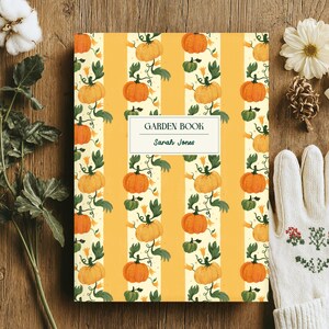 Może przedstawiać: Twarda oprawa książki ogrodniczej z żółtym wzorem w paski z dyniami. Na okładce widnieje napis "GARDEN BOOK" i "Sarah Jones". Biała rękawica z haftem kwiatowym, kwiat bawełny i zieleń ułożone na drewnianej powierzchni.
