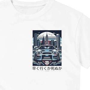Puede incluir: Camiseta blanca con un gráfico de un coche azul frente a un horizonte urbano. El texto "早く行くか死ぬか" está impreso debajo del coche.