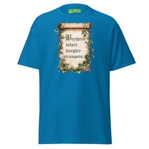 Op de afbeelding: Een felblauw T-shirt met korte mouwen en een centrale afbeelding van een verouderde, opgerolde perkamentrol omstrengeld met groene klimopranken. De tekst op de rol luidt Brethren before haughty strumpets, geschreven in een zwart gotisch lettertype.