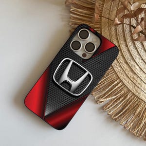 Op de afbeelding: Zwarte en rode telefoonhoes met een zilveren Honda-logo. De hoes heeft een koolstofvezeltextuur en een rood gradiëntontwerp. De telefoonhoes is ontworpen voor een smartphone.